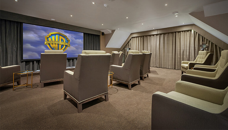 Cinema room with large comfortable chairs, a projector screen displaying the Warner Bros logo, and ambient lighting