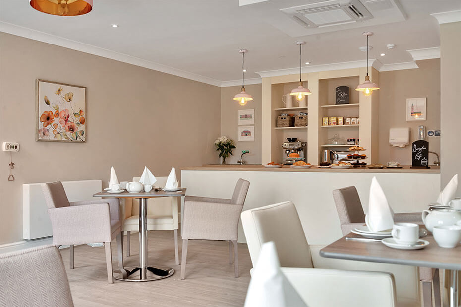 A modern cafe interior with neatly arranged tables and chairs, white tablecloths, pendant lights, and a serving counter in the background