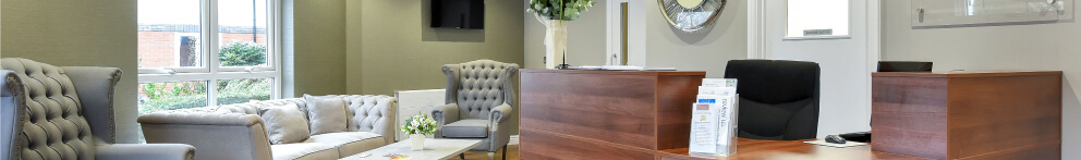 A modern reception area with a wooden desk, grey armchairs, a sofa, and a wall-mounted television