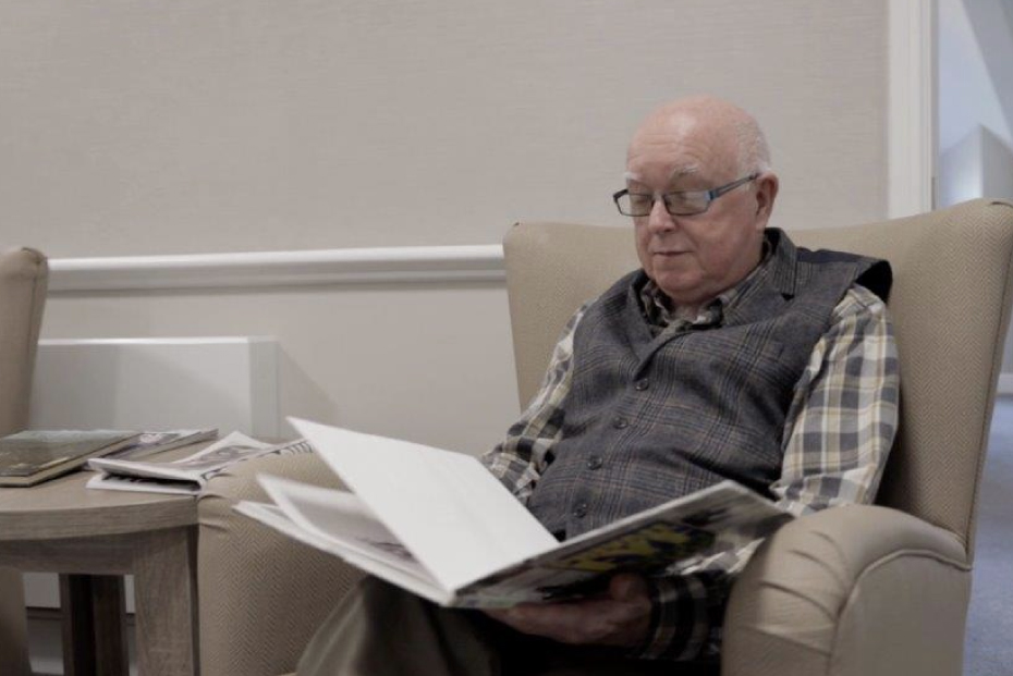 An older man reading a book whilst sat in an armchair